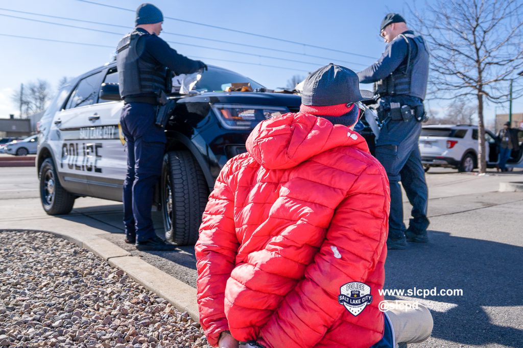 a person in hand restraints sitting near police officers