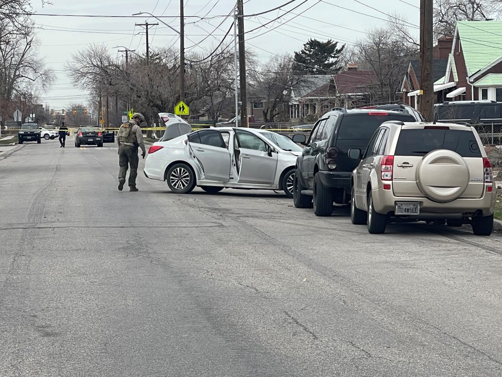 Photo of a car crash and a police officer in a bomb suit.