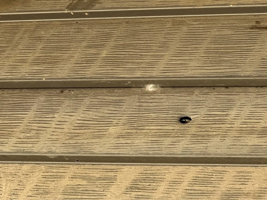 Photo of a bullet hole in the side of a house.